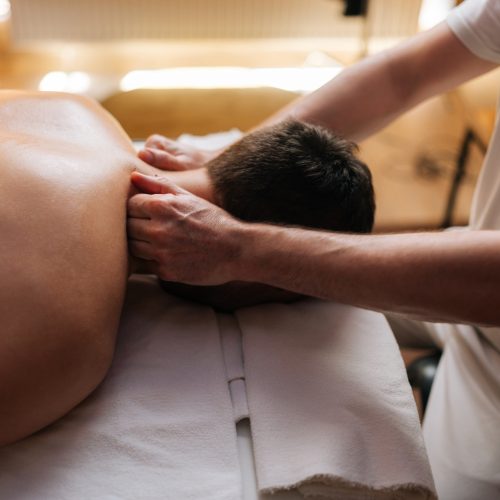 Closeup side view head of unrecognizable young relaxed man lying down on massage table during shoulder and neck massage at spa salon.